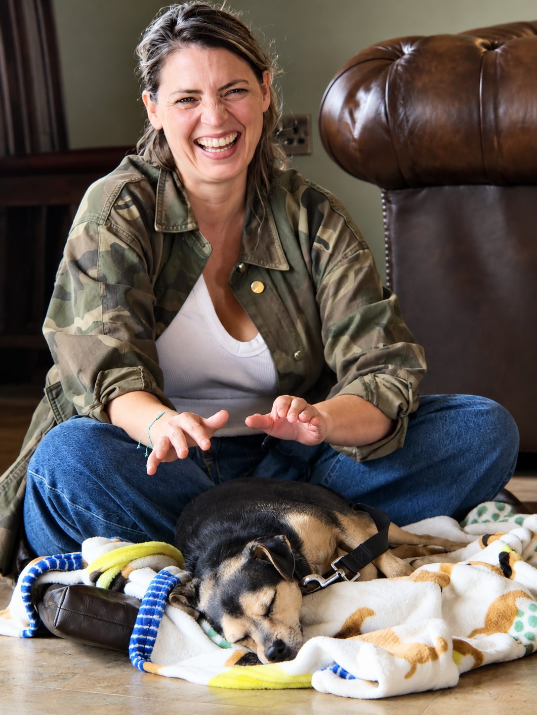 A guardian laughing warmly while her dog sleeps soundly on a blanket in front of her